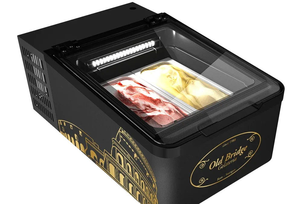 Das Bild zeigt eine Mini-Eistruhe im Old-Bridge-Design – kompakt, mit Glasdeckel und integrierter LED-Beleuchtung. Sichtbare Gelato-Schalen, schwarzes Gehäuse mit goldenen Markenelementen.